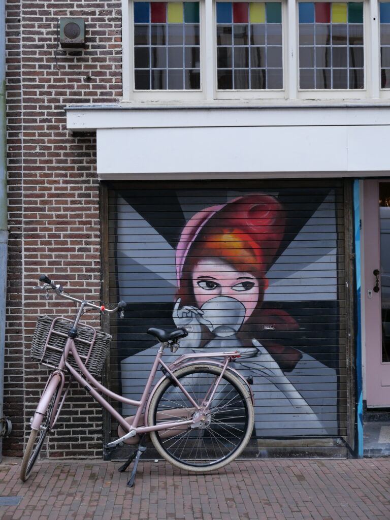 Ένα ροζ ποδήλατο μπροστά σε τοιχογραφία γυναίκας που πίνει καφέ σε τοίχο του Amersfoort