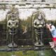 Προσκυνητής με κόκκινο σαρόνγκ πλένεται σε πηγή με αγάλματα έξω από τον ναό στο Ουμπούντ